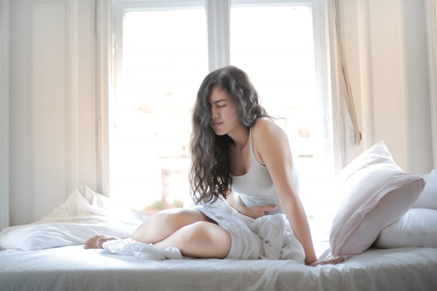 Woman In Gray Tank Top While Sitting On Bed