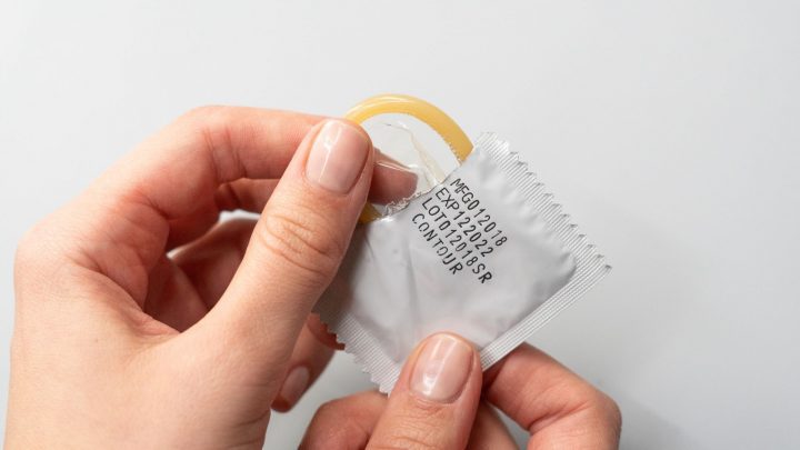 Person pulling condom out of package with expiration date